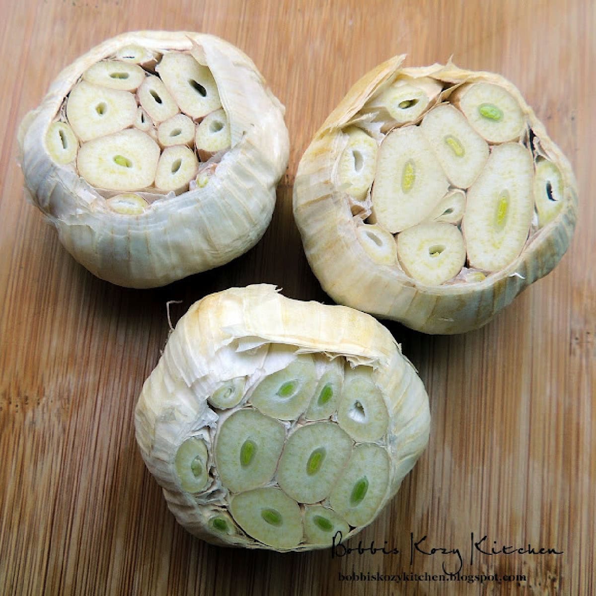 Three heads of garlic that have the very ends cut off to expose the cloves inside on a wooden cuttin gboard.