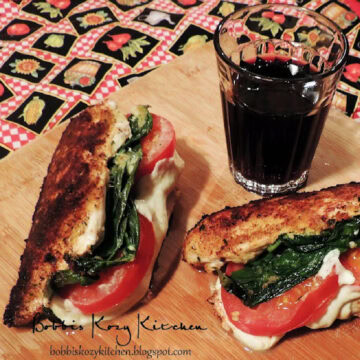 Two caprese stuffed chicken breasts with a glass of red wine on a wooden cutting board.