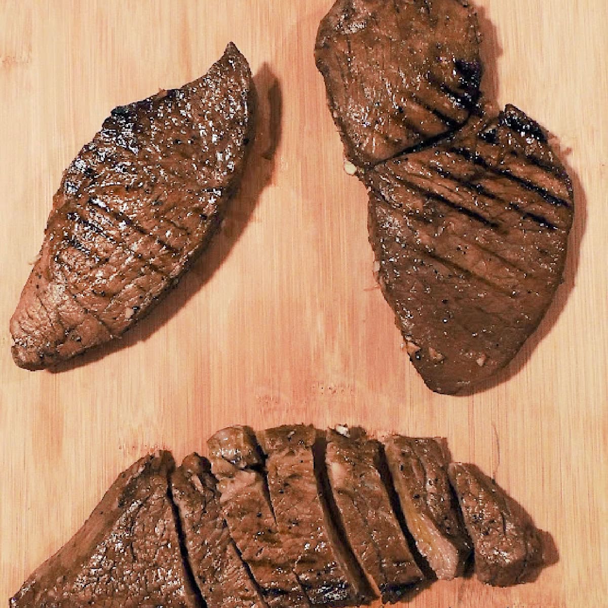 Overhead view of three grilled steaks on a wooden cutting board that were marinated in this balsamic red wine steak marinade.