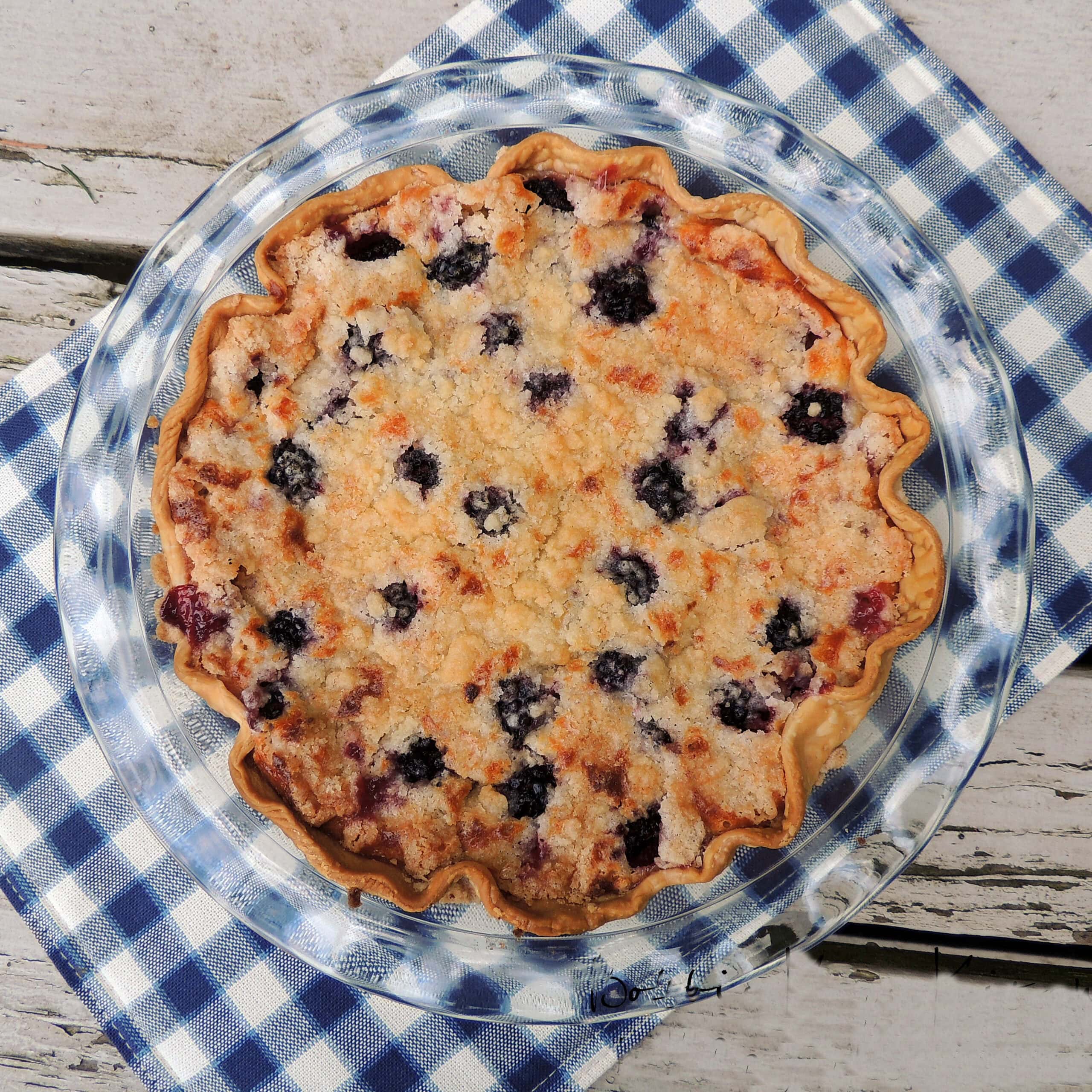 overhead view of a low-carb blackberry custard pie on a blue and white checkers placemat sitting on a wooden background.