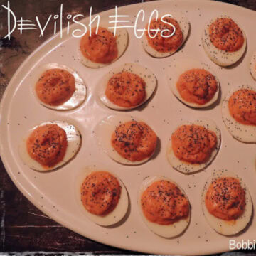 A white deviled egg platter on a dark table with "devilish" eggs in it.