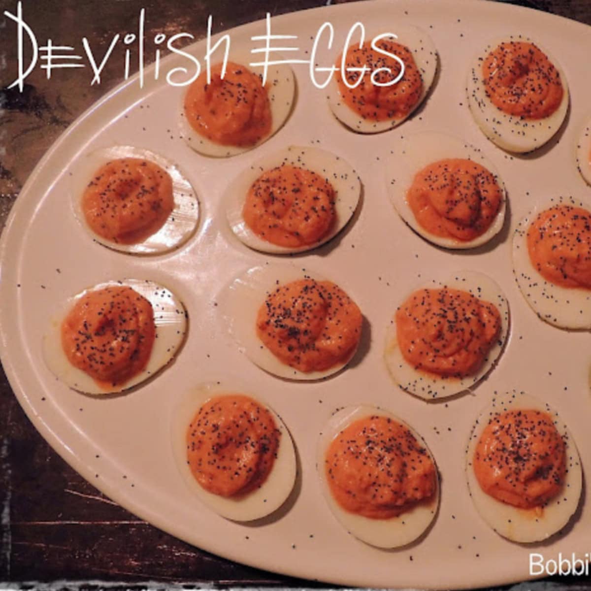 A white deviled egg platter on a dark table with "devilish" eggs in it.