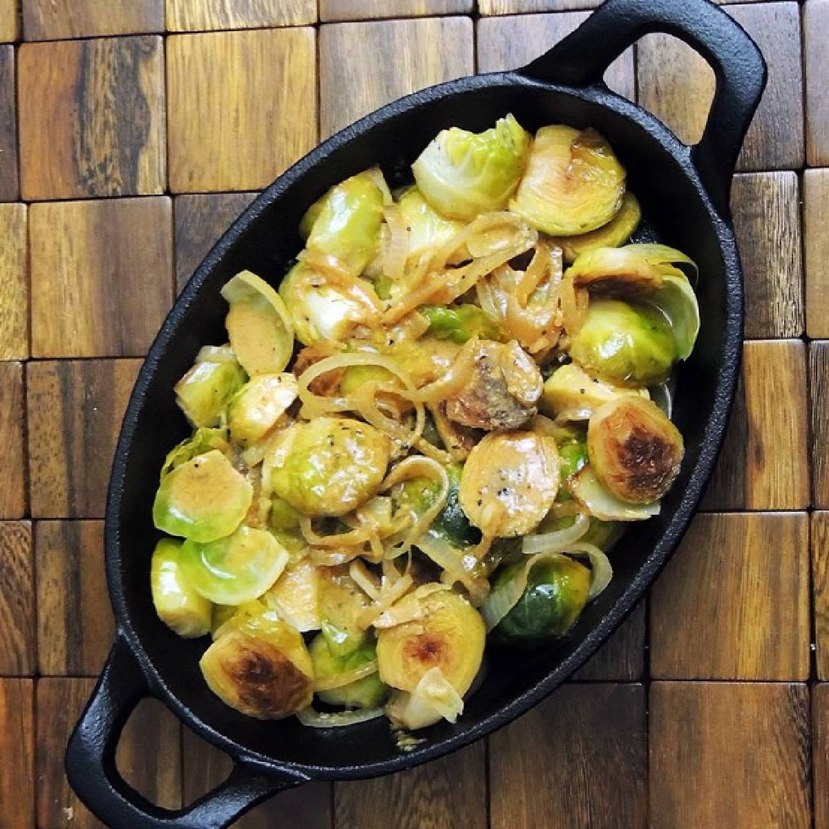 Overhead view of a small cast iron casserole dish with White Wine Braised Brussels Sprouts in it on a wooden placemat.