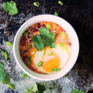 Baked eggs and salsa with cheese and cilantro in a white ramekin.