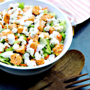 Buffalo chicken chopped salad in a white bowl with wooden salad tongs next to it.