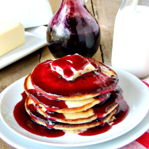 A stack of pancakes topped with butter and sugar-free keto blueberry syrup on a white plate.