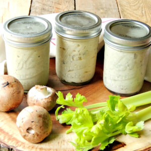 Three mason jars of homemade cream of mushroom, celery, and chicken soup on a wooden cutting board with fresh veggies.