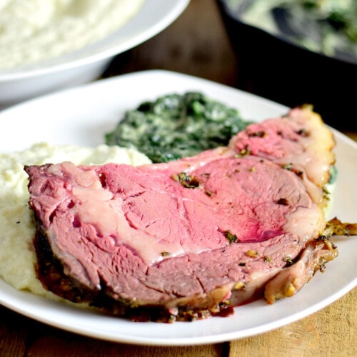 A slice of rib roast with garlic herb butter on a white plate with mashed cauliflower and creamed spinach.