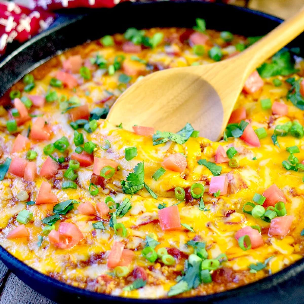 Mexican cauliflower rice in a cast iron skillet topped with lots of melted cheese, fresh chopped tomatoes, green onions, and cilantro.