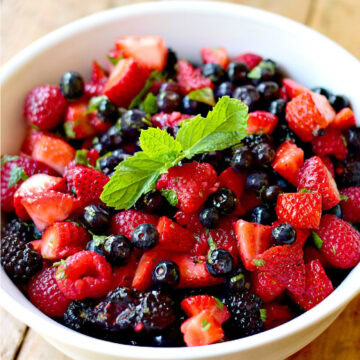 Low-carb mixed berry salad in a yellow bowl with white interior on a wooden table. The salad is topped with a sprig of fresh mint.