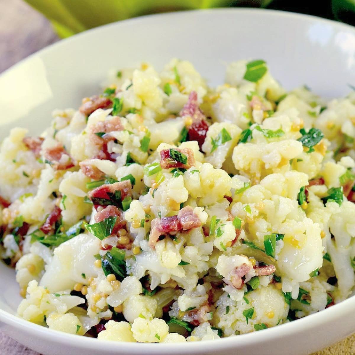 A large salad bowl full of cauliflower salad with bacon and a mustard seed vinaigrette.