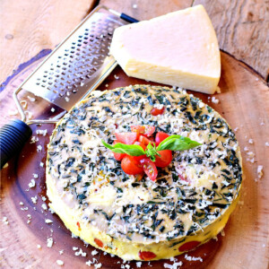 Instant pot caprese frittata on a wooden cutting board with a wedge or parmesan cheese and a cheese grater.