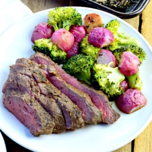 Steak, broccoli, and radishes cooked on a sheet pan served on a white plate.