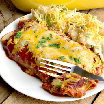 Two low carb beef enchiladas on a white plate with a side salad. The plate is on a wooden table and you can see the yellow baking dish that holds the rest of the enchiladas in the background.