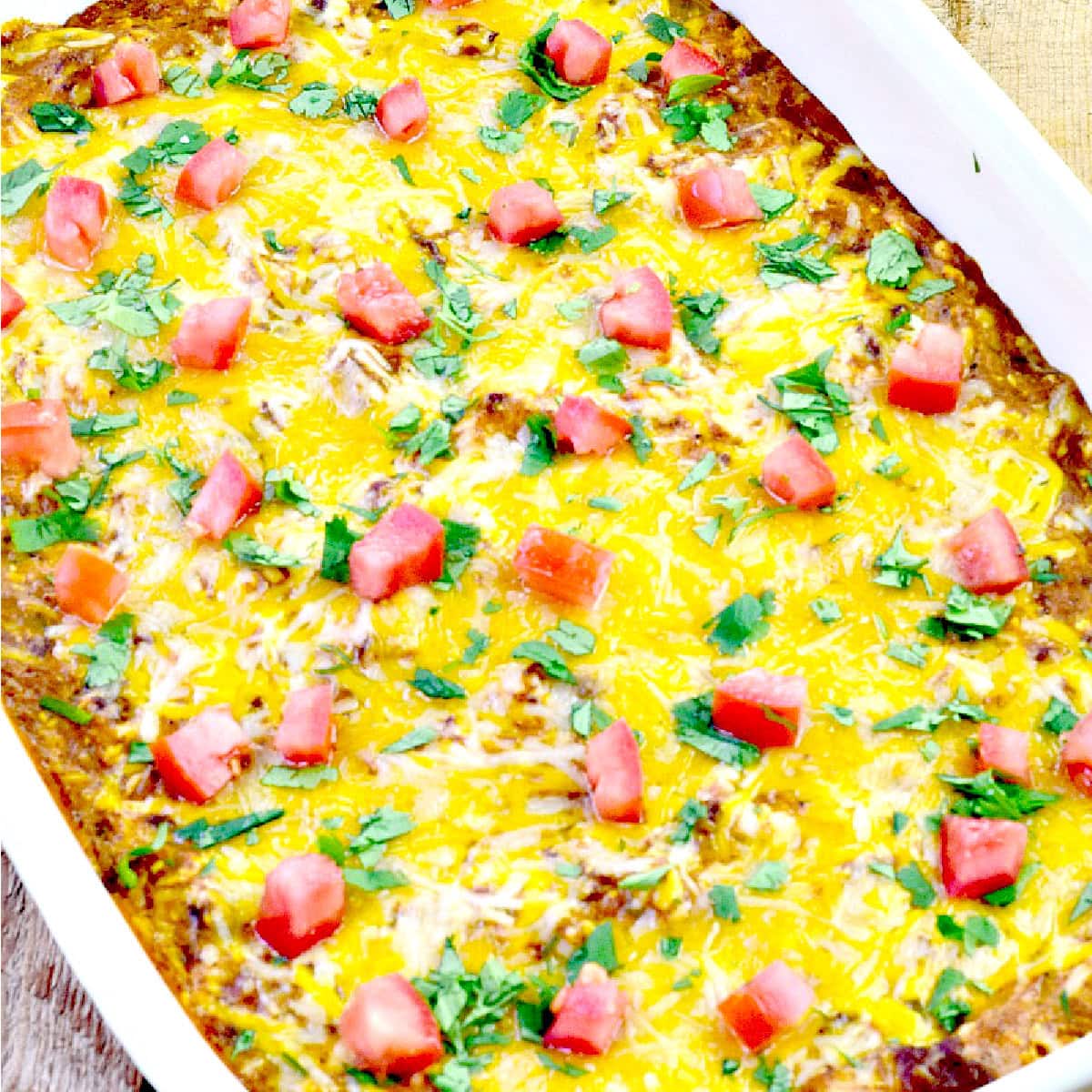 Low-carb Texas Trash Dip in a white baking dish topped with chopped tomatoes and cilantro.
