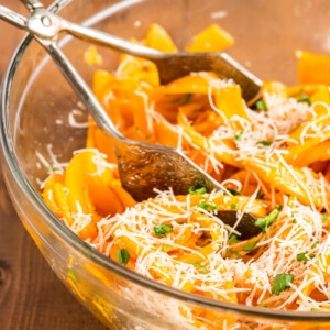 Butternut squash noodles with browned butter and parmesan in a glass bowl with silver tongs.