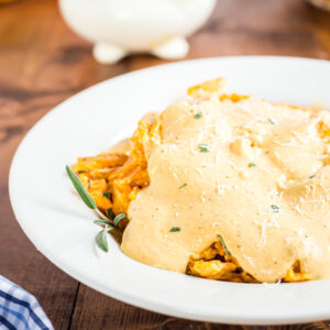 Image of a white bowl filled with keto and gluten-free noodles covered with a delicious Pumpkin Alfredo Sauce. The bowl is placed on a wooden table, and the dish is garnished with some herbs and spices. The noodles look creamy, and the sauce appears to have a smooth texture.