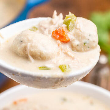 A white ladel full of keto chicken and dumplings over a white bowl.