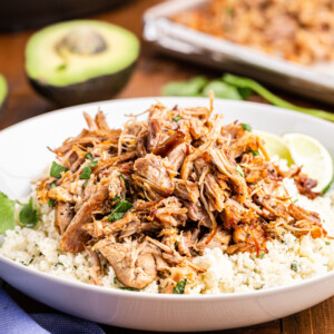 Easy Keto Pork Carnitas in a white bowl with cauliflower rice and a lime wedge.