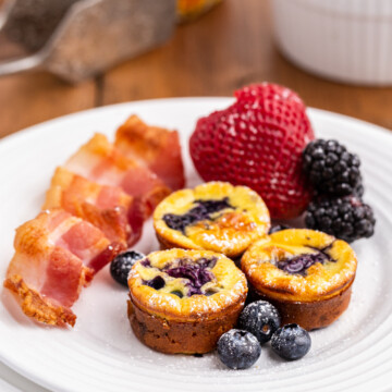 Mini keto pancake bites on a white plate with berries and bacon.