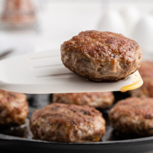 Keto country breakfast sausage in a cast iron skillet with one patty on a white spatula.