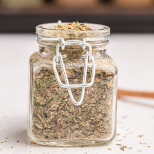 Homemade Italian seasoning in a glass spice jar on a white counter.