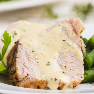 a slice of Pork Tenderloin with a Creamy Herb Mustard Sauce on a white plate.