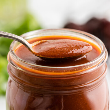 Homemade red chile enchilada sauce in a mason jar with a silver spoon.