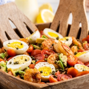 Low carb shrimp Louie salad in a wooden salad bowl with wooden salad tongs.