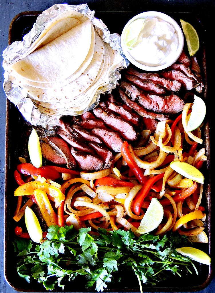 Overhead view of keto sheet pan steak fajitas with keto tortillas, sour cream, and fresh cilantro on the baking sheet.