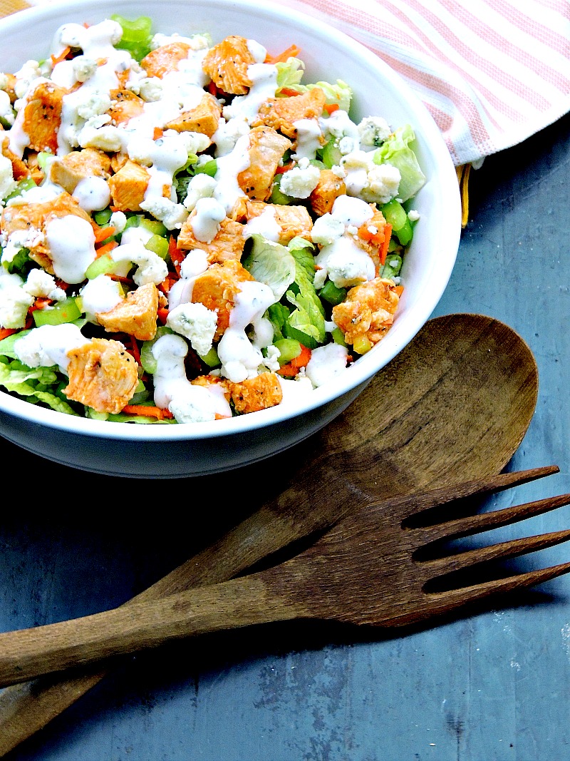 Buffalo chicken chopped salad in a bowl on a blue wooden table with wooden salad tongs next to the bowl.