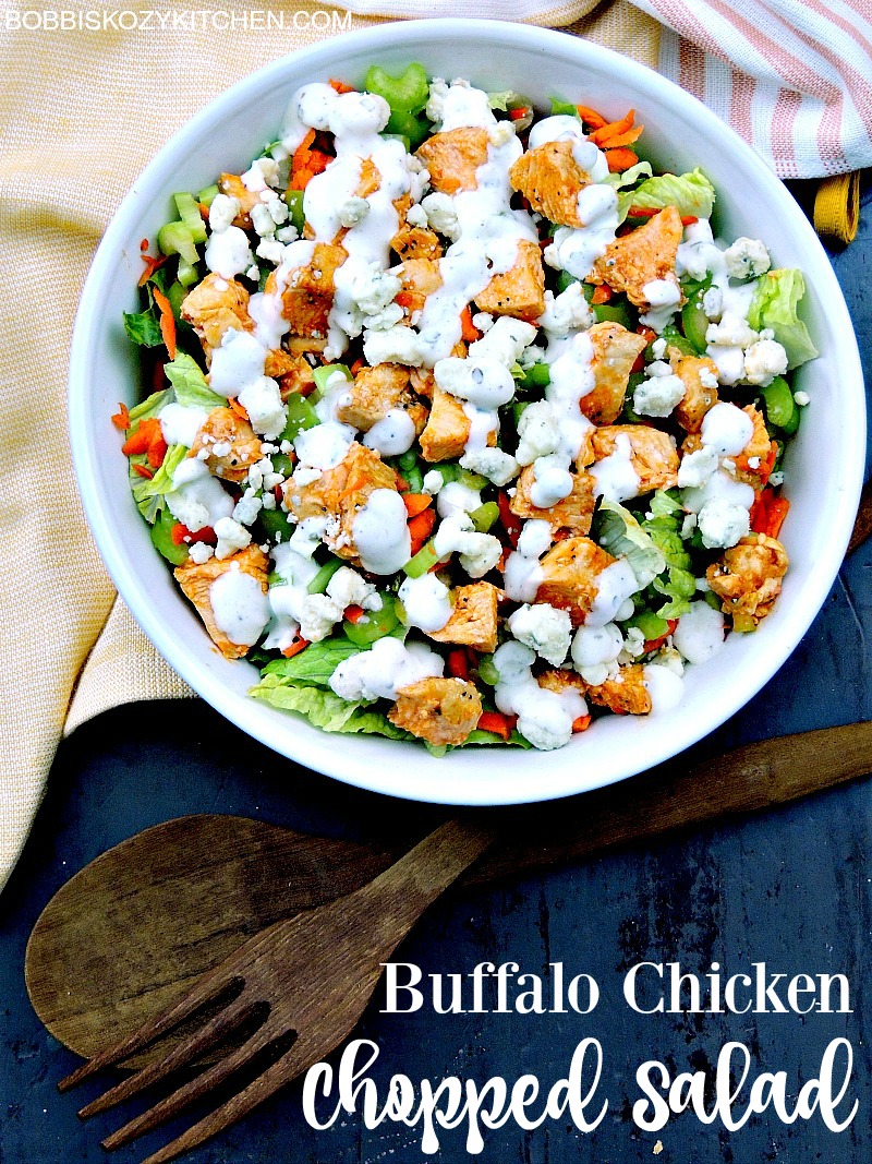 Buffalo chicken chopped salad in a white bowl with wooden salad tongs on a blue wooden table.