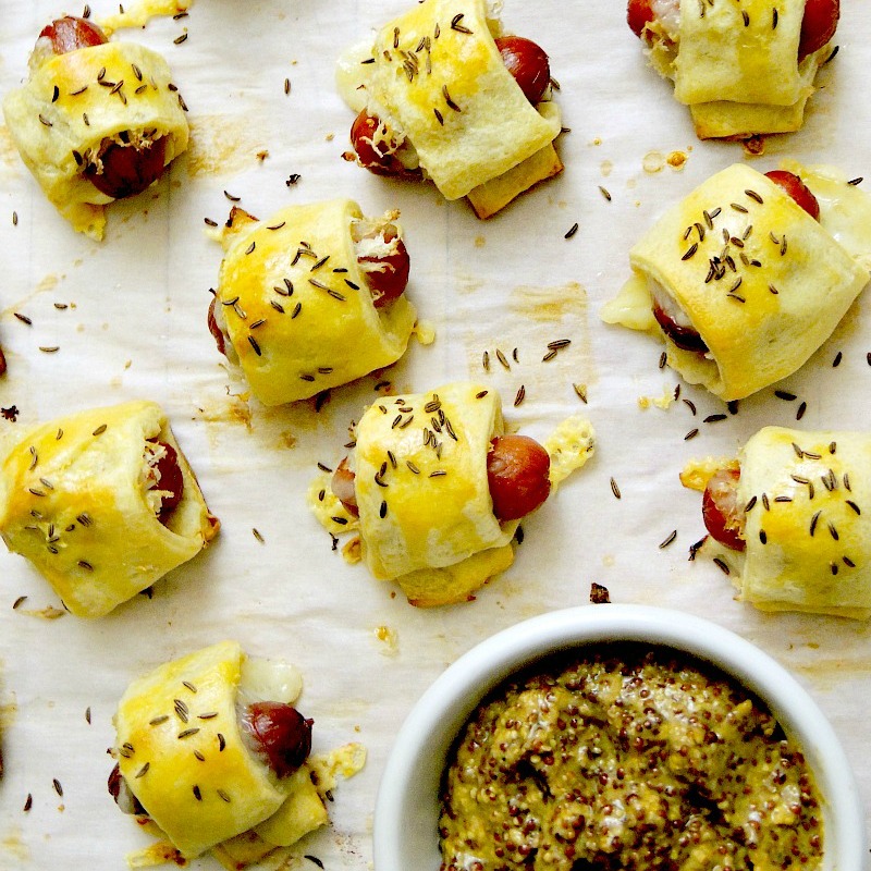 Mini Reuben Pigs in a Blanket on a white background with whole grain mustard