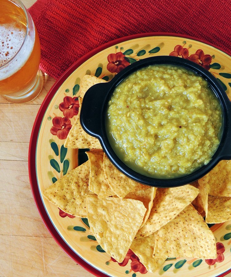 Overhead view of a black bowl full of Roasted Tomatillo Salsa on a Mexican inspired plate with keto tortilla chips.