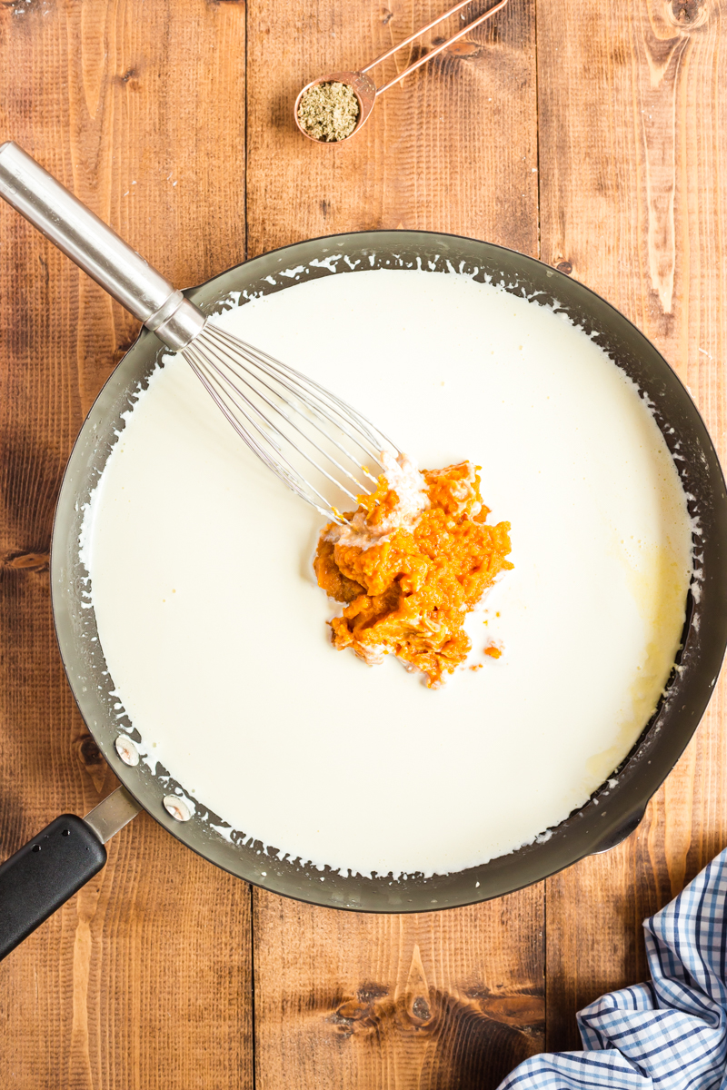 Overhead photo of cream being heated in a skillet and adding pumpkin puree to it.
