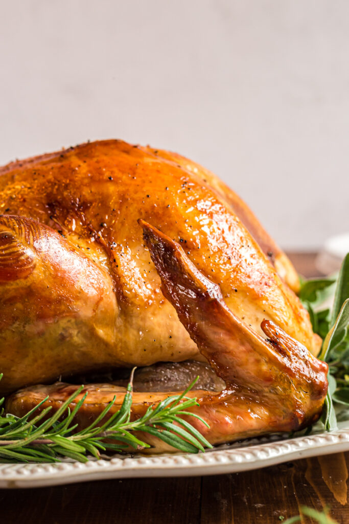 Side view of a perfectly roasted turkey on a white serving platter.
