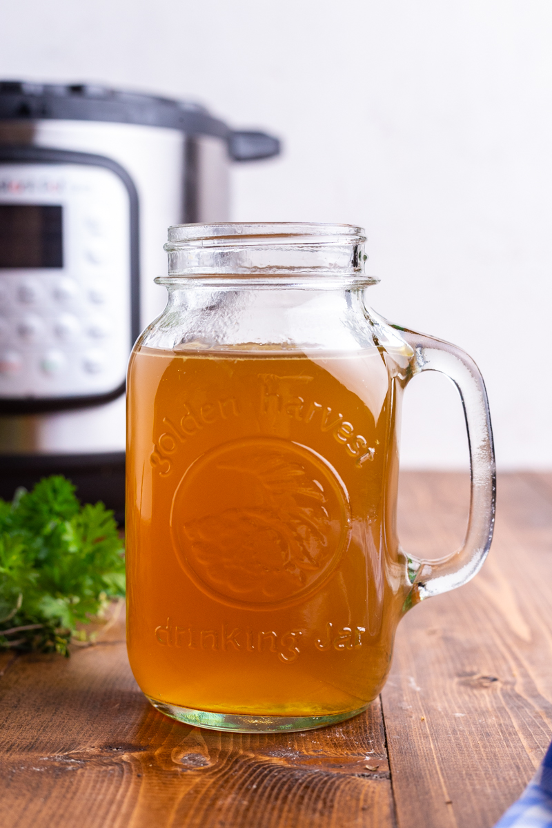Photo of a mason jar full of homemade turkey bone broth on a wooden table with an Instant Pot in the background.