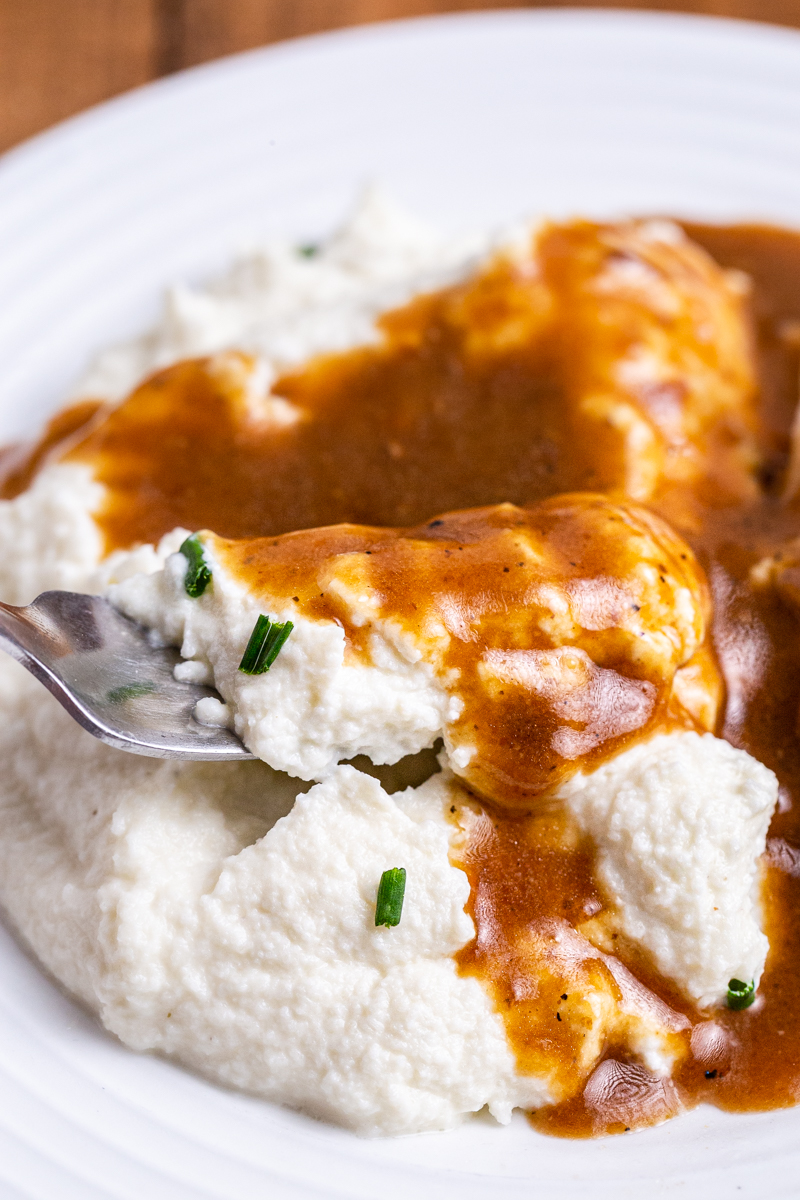 Image is of keto turkey gravy over mashed cauliflower on a white plate.