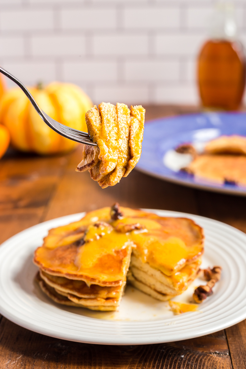 Low carb pumpkin pie pancakes on a white plate with a bite full on silver fork closer to the camera.