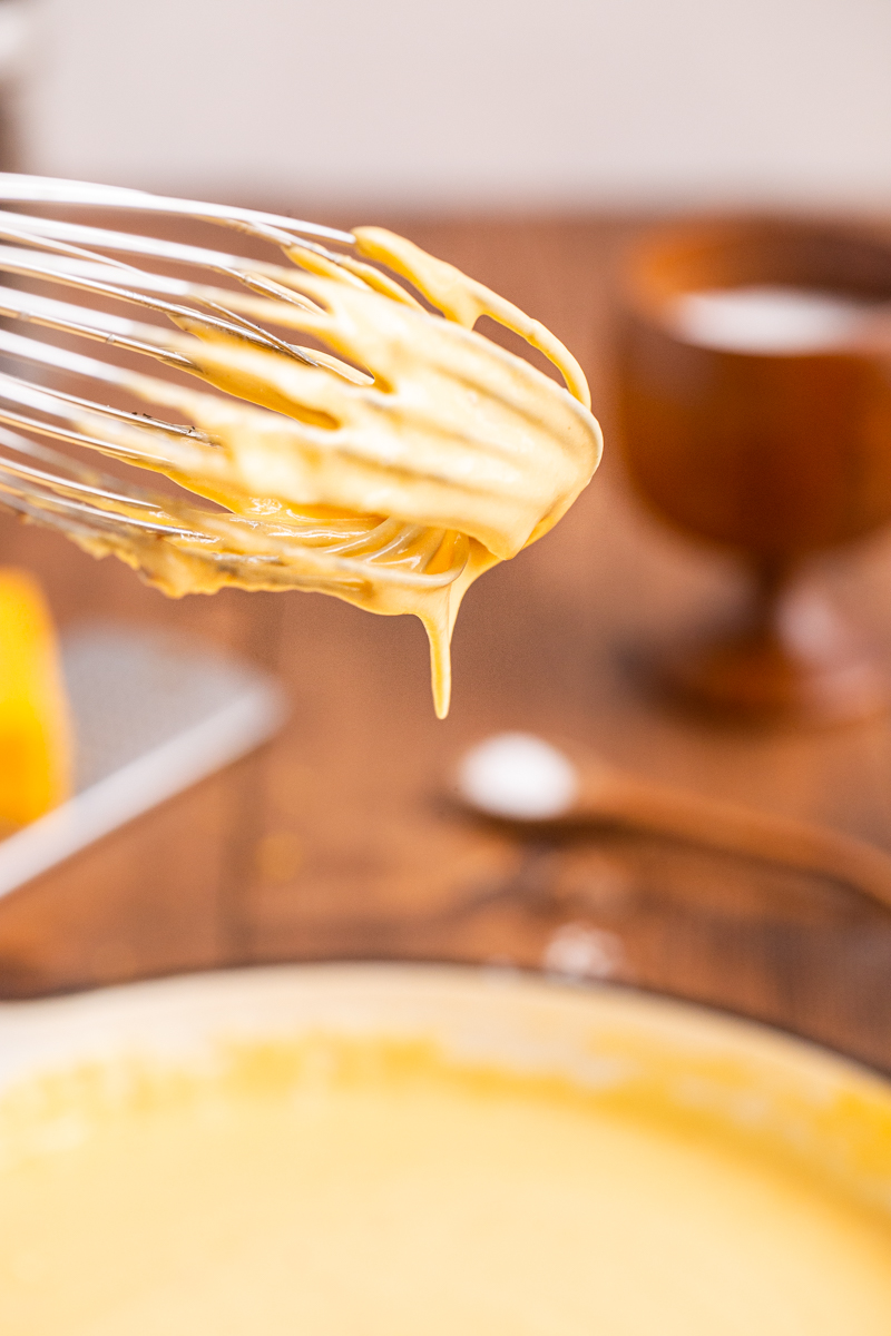 Close up photo of a whisk coated with Easy Keto Cheese Sauce above a skillet.