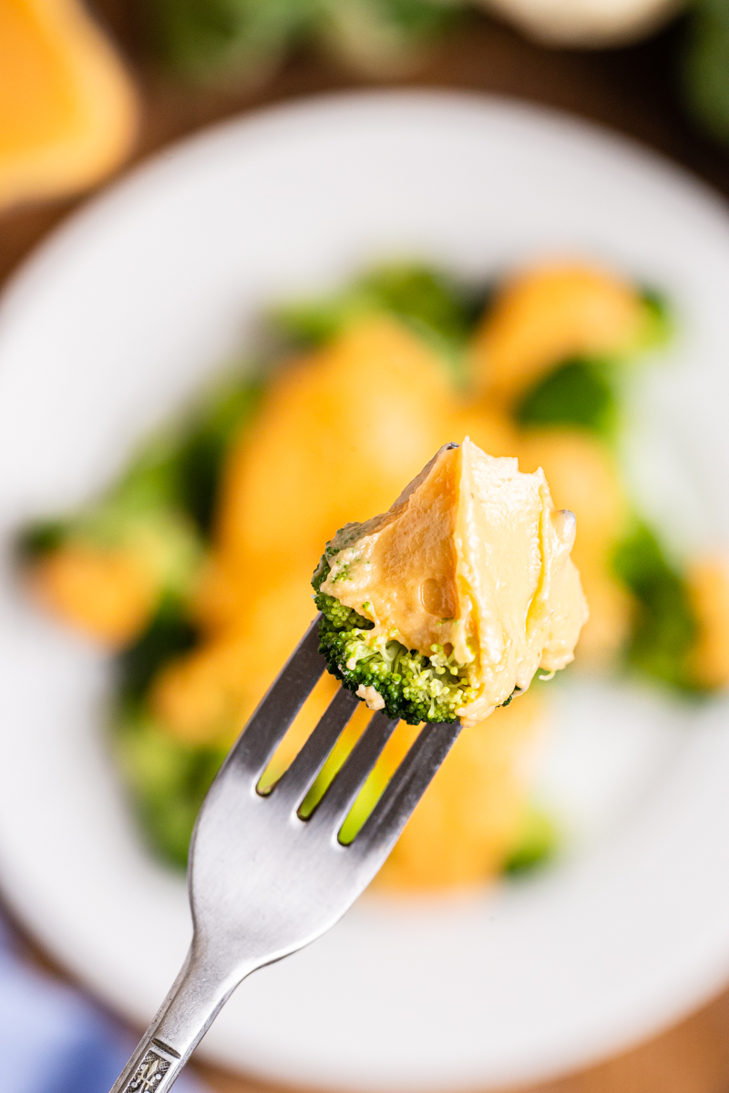 Close up photo of a broccoli floret on a fork coated with Easy Keto Cheese Sauce.