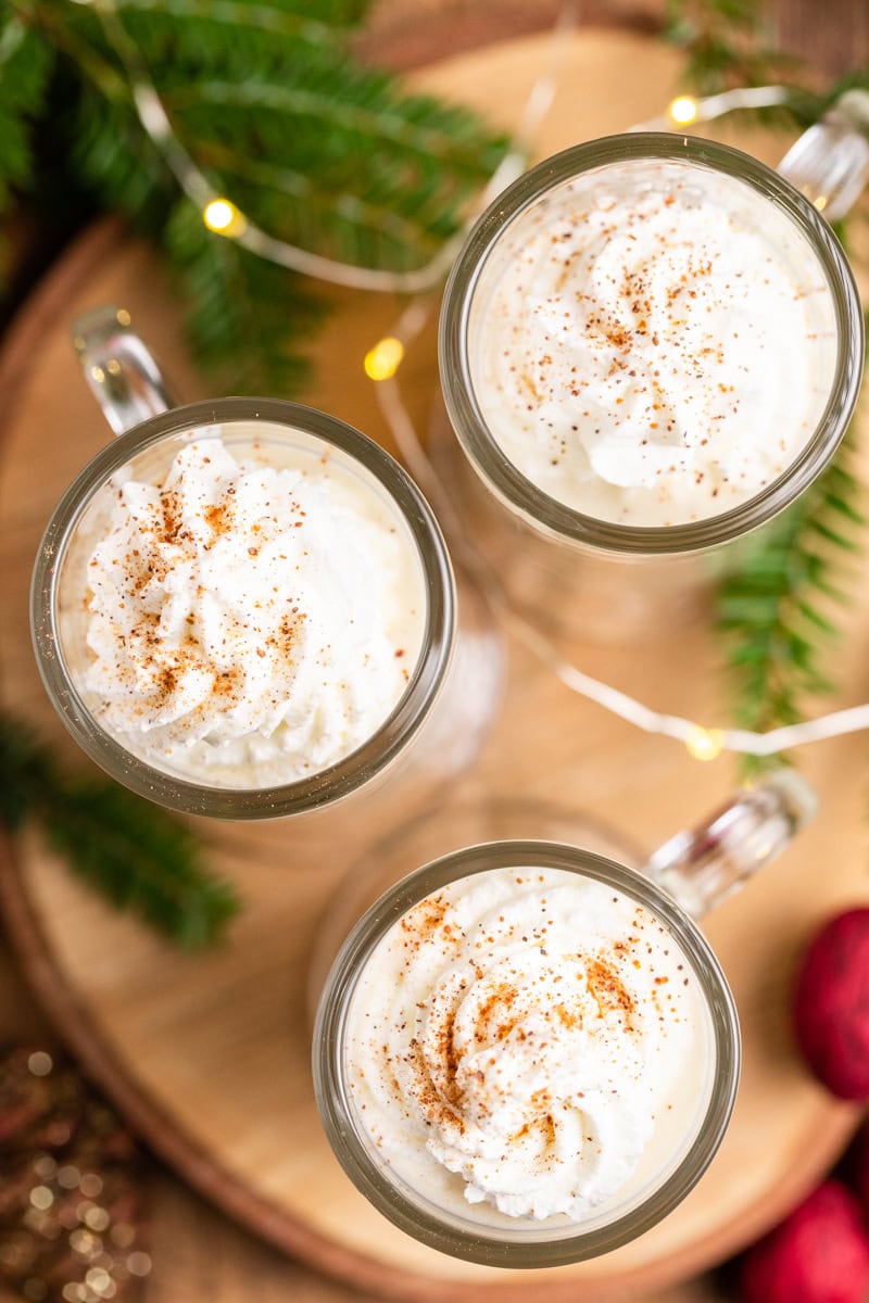 Overhead photo of 3 mugs of Keto Eggnog (Dairy-Free & Sugar-Free) on a round wooden cutting board.