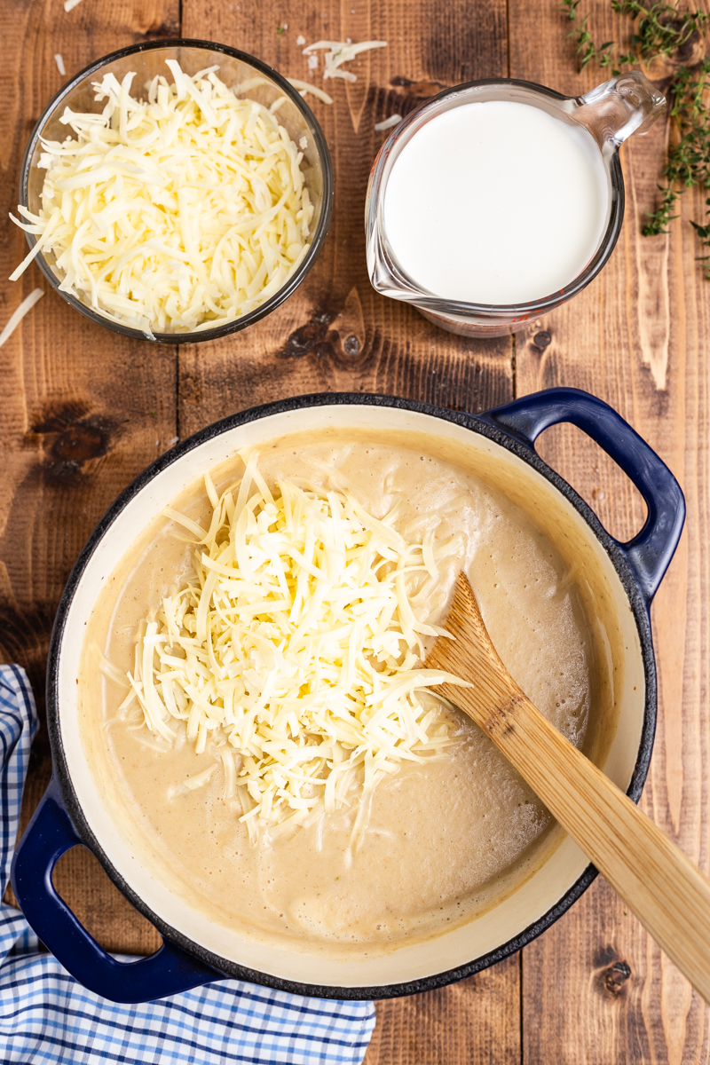 Overhead photo of Easy Cauliflower Cheese Soup in a large blue soup pot with shredded cheese being stirred in.