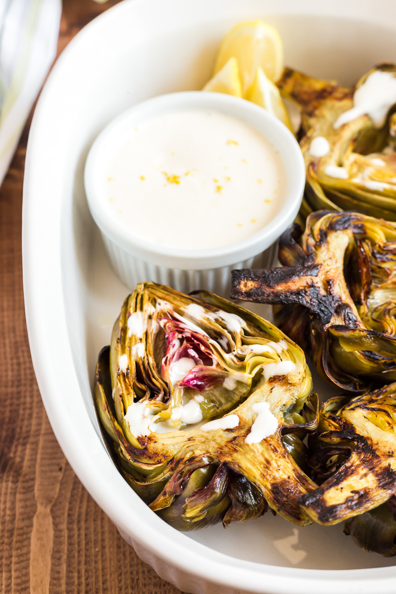 Photo of grilled artichokes with with lemon garlic sauce in a white baking dish.