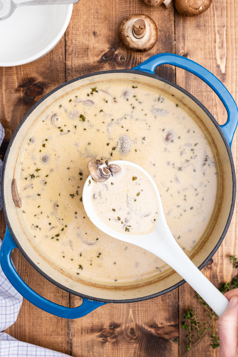 Overhead photo of Keto Cream of Mushroom Soup in a large blue soup pot on a wooden table with a ladle full closer to the camera.
