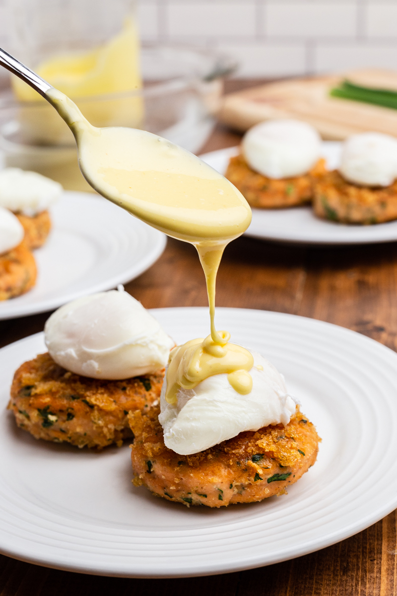 Closeup photo of a spoon drizzling hollandaise sauce over the poached eggs on Keto Salmon Eggs Benedict.
