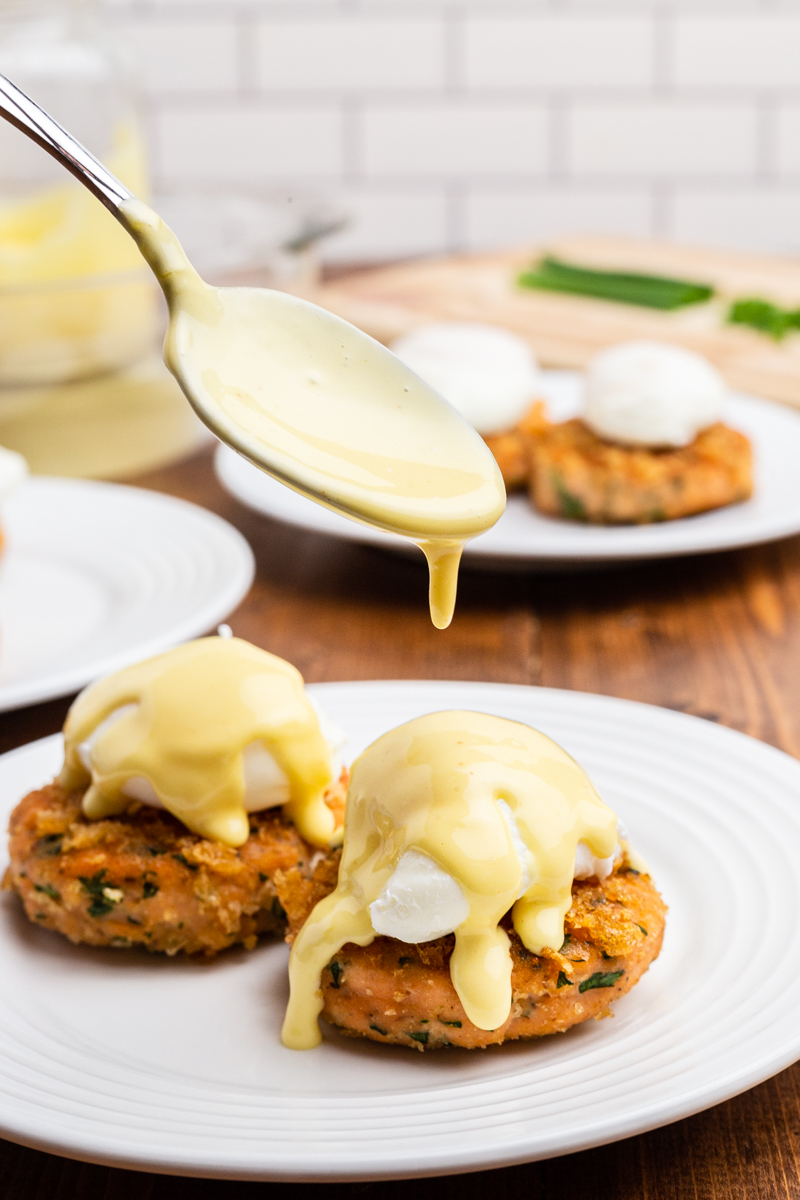 Closeup photo of Keto Salmon Eggs Benedict on a white plate with a spoon drizzling hollandaise sauce on top.