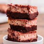 Keto Red Velvet Cheesecake Brownies stacked on top of each other on a white plate.