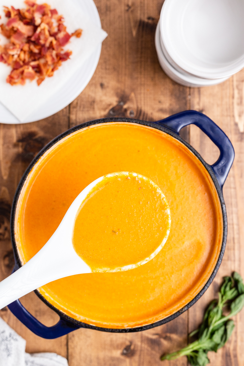 Overhead photo of Keto Tomato Bisque with Bacon in a large blue soup pot with a ladle full closer to the camera.
