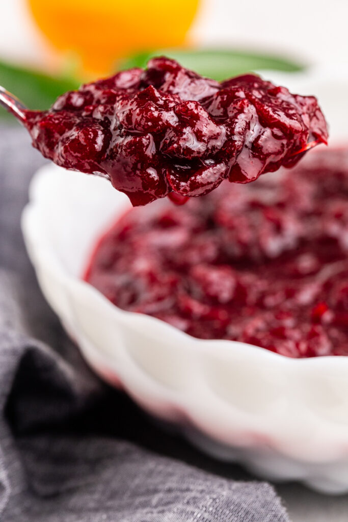 Keto Cranberry Sauce in a white bowl with a silver serving spoon dishing some up.
